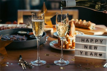 Champagne glasses filled on wood table with small plates (tapas) and Happy New Year sign.