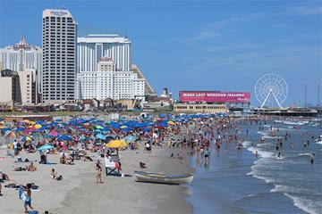 Atlantic City Beach and Boardwalk along the shoreline with beach goers, umbrellas, lifeguard stand and boat. Atlantic City, NJ.