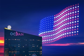 Ocean Casino Resort and American Flag made out of drones flying high in sky with ocean and sunset in distance.